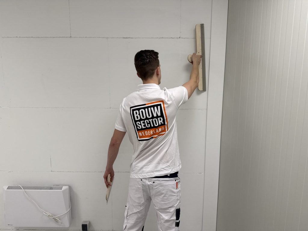 Stukadoor van Bouwsector Nederland zet een brede spaan tegen een wand met zichtbare naden