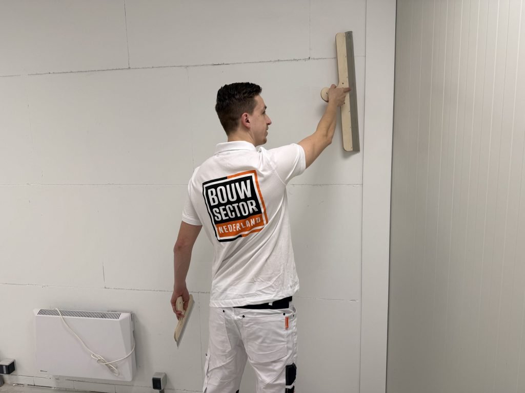 Stukadoor van Bouwsector Nederland trekt een brede spaan langs een wand met zichtbare naden